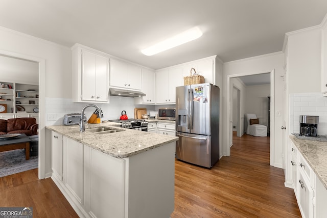 kitchen with stainless steel appliances, a sink, under cabinet range hood, white cabinetry, and wood finished floors