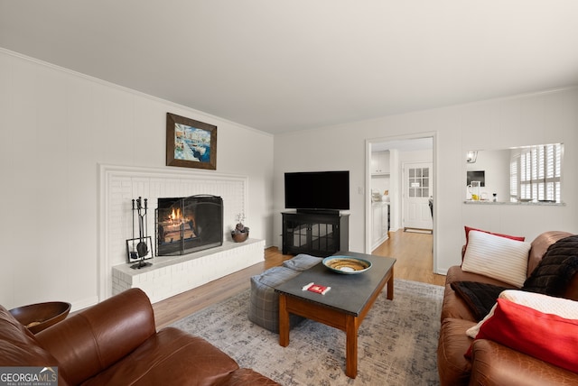 living area featuring light wood-style flooring, ornamental molding, and a brick fireplace