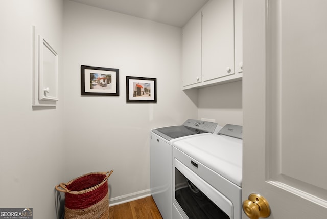 clothes washing area featuring cabinet space, washing machine and clothes dryer, wood finished floors, and baseboards