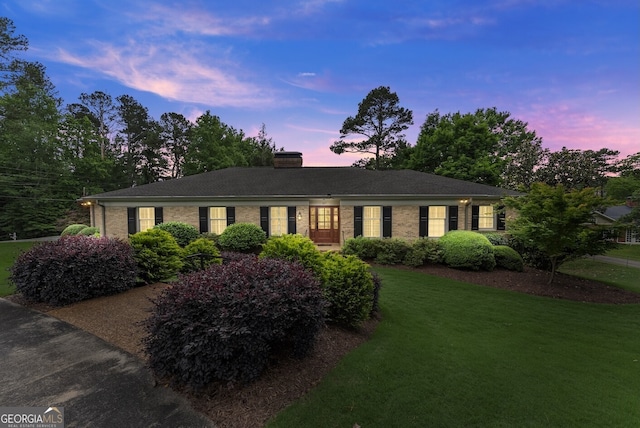 single story home featuring a lawn, a chimney, and brick siding