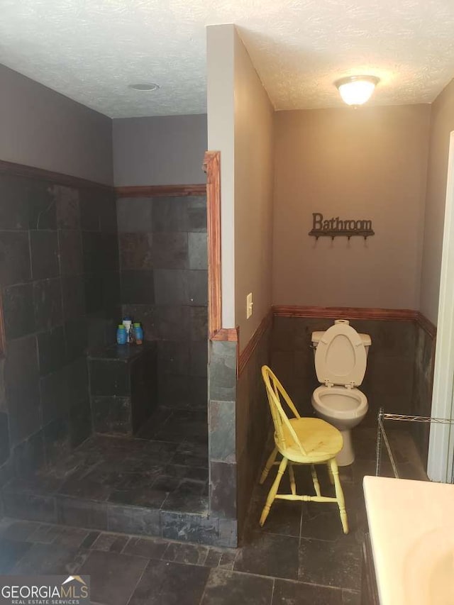 1383 Sims Rd SE, Winder, GA 30680 - bathroom with a textured ceiling, toilet, a wainscoted wall, a tile shower, and tile walls