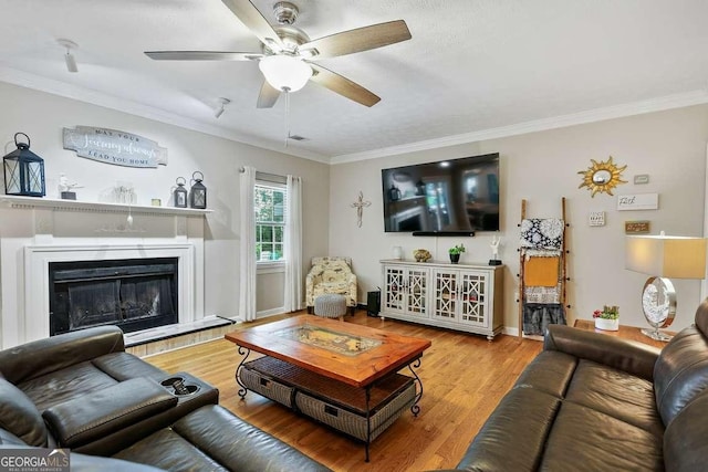 living room with ceiling fan, crown molding, wood finished floors, a glass covered fireplace, and baseboards
