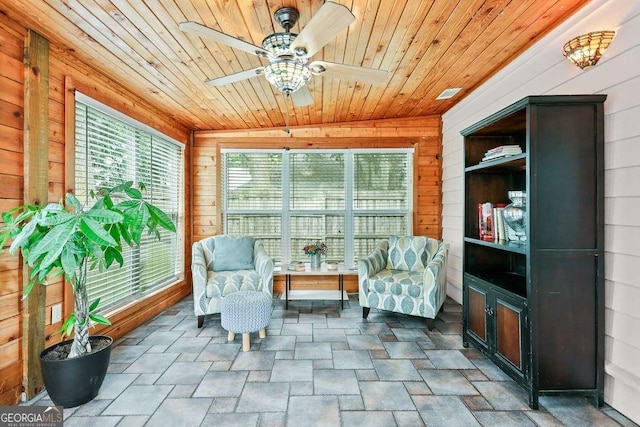 sitting room featuring wooden walls, wood ceiling, stone finish flooring, and ceiling fan