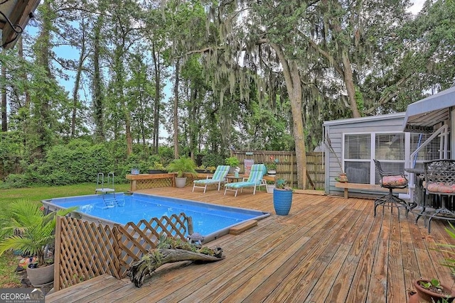 outdoor pool with a deck, fence, and view of wooded area