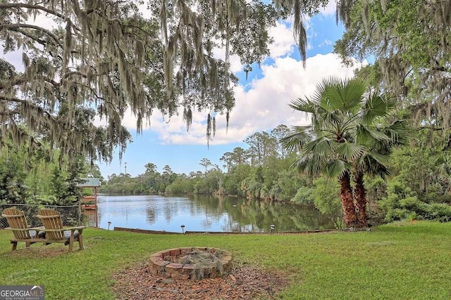 view of green lawn featuring an outdoor fire pit, a water view, and a forest view
