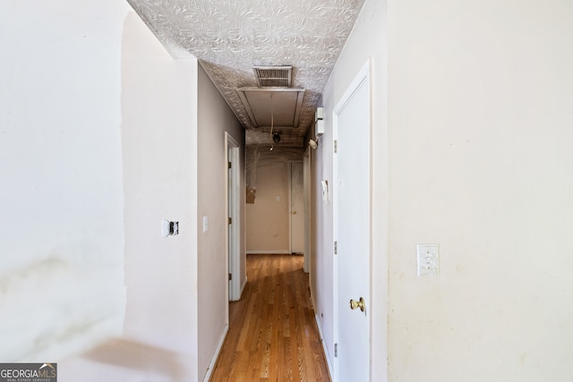 corridor with attic access, light wood-style flooring, and a textured ceiling