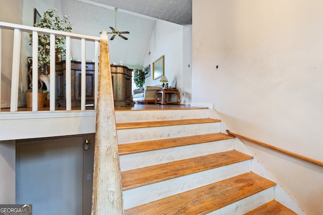 stairway with ceiling fan, vaulted ceiling, and a textured ceiling