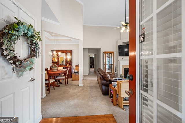foyer entrance featuring ornamental molding, ceiling fan, a towering ceiling, light colored carpet, and a chandelier