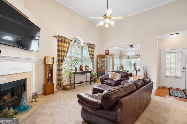 carpeted living room with a ceiling fan, a towering ceiling, ornamental molding, a fireplace with flush hearth, and baseboards