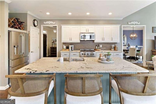 kitchen with high end appliances, a sink, white cabinets, a kitchen breakfast bar, and crown molding