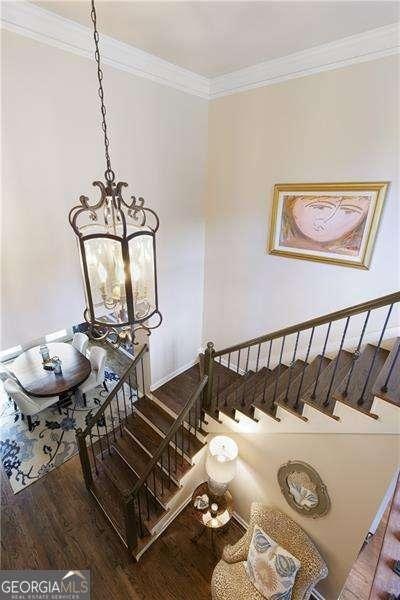 stairs featuring ornamental molding, wood finished floors, and a chandelier