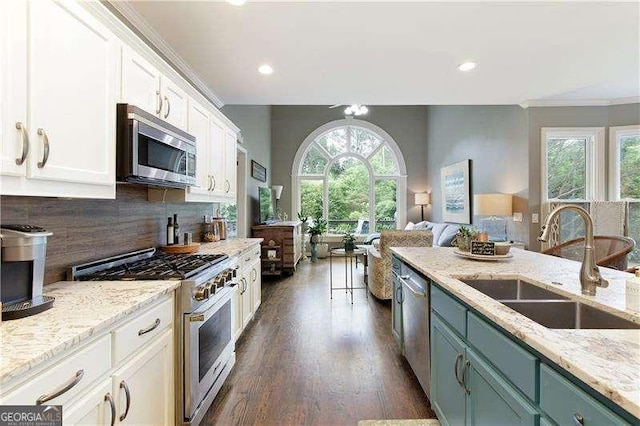 kitchen featuring stainless steel appliances, a sink, white cabinetry, backsplash, and open floor plan