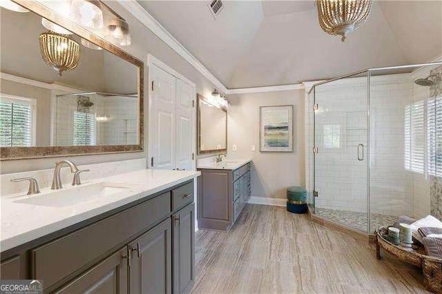 full bath featuring ornamental molding, a stall shower, vaulted ceiling, wood finished floors, and two vanities