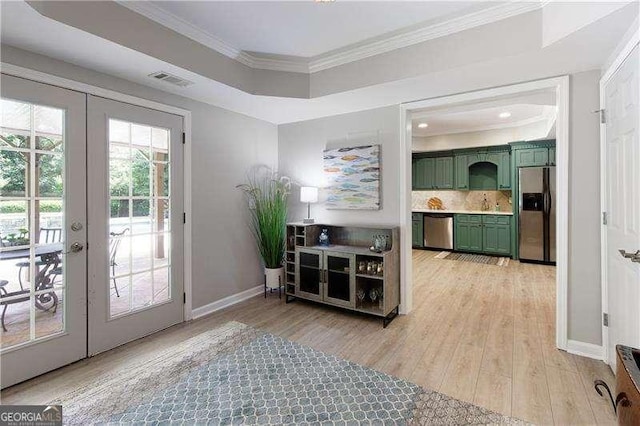 doorway with french doors, ornamental molding, baseboards, light wood-style flooring, and a raised ceiling
