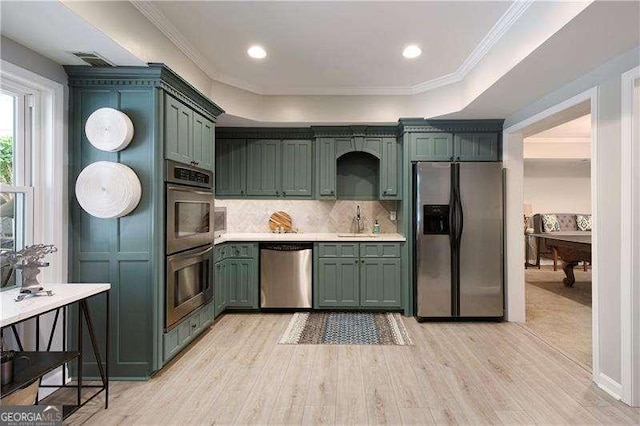 kitchen with appliances with stainless steel finishes, a sink, green cabinets, light countertops, and light wood-style flooring
