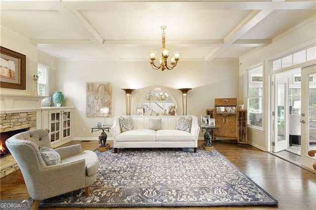 living room featuring a chandelier, coffered ceiling, wood finished floors, a stone fireplace, and baseboards