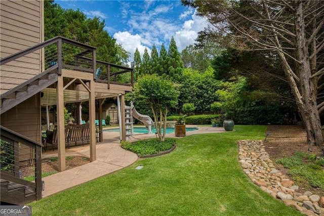 view of grassy yard featuring a deck, a patio area, and an outdoor pool