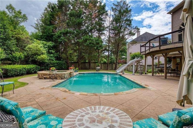 view of swimming pool with a water slide, a patio area, a fenced backyard, and a pool with connected hot tub