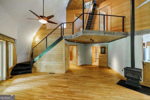 218 Wedgewood Dr, Danielsville, GA 30633 - unfurnished living room with a towering ceiling, wooden walls, a wood stove, stairs, and wood finished floors