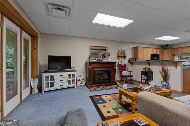 living room featuring a drop ceiling, carpet floors, and a glass covered fireplace