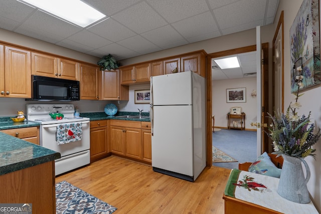 kitchen with white appliances, a paneled ceiling, a sink, dark countertops, and light wood-style floors