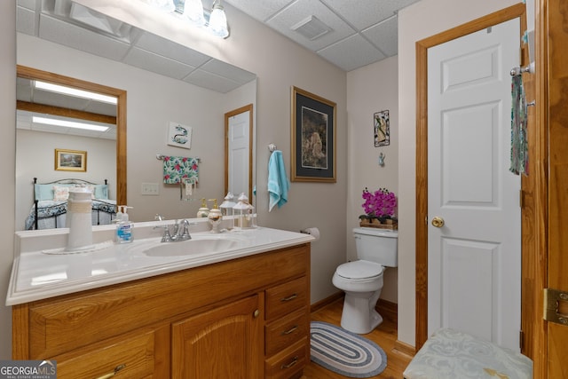 bathroom featuring a paneled ceiling, wood finished floors, toilet, and vanity