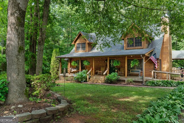 view of front of home with a porch, a chimney, a front yard, log siding, and roof with shingles