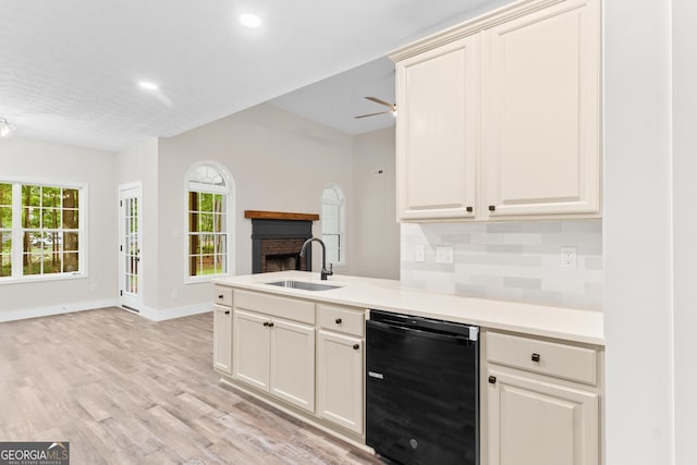 kitchen with a sink, a brick fireplace, light wood-type flooring, dishwasher, and a peninsula