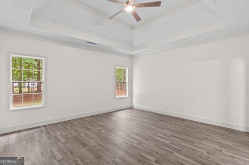 spare room featuring a tray ceiling, wood finished floors, a ceiling fan, baseboards, and ornamental molding