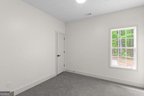 spare room featuring dark colored carpet and baseboards