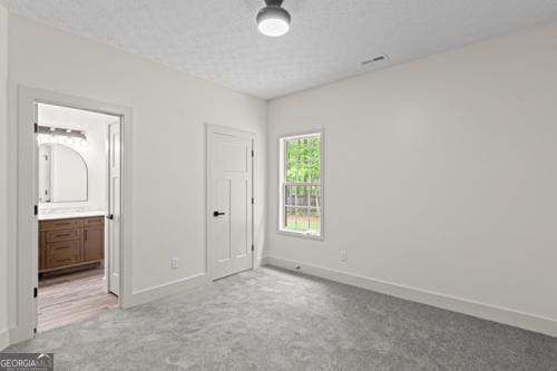 unfurnished bedroom featuring light colored carpet, baseboards, and ensuite bathroom