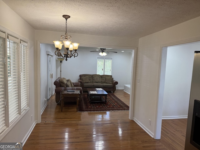 living room with dark wood-type flooring, a chandelier, a textured ceiling, a ceiling fan, and baseboards