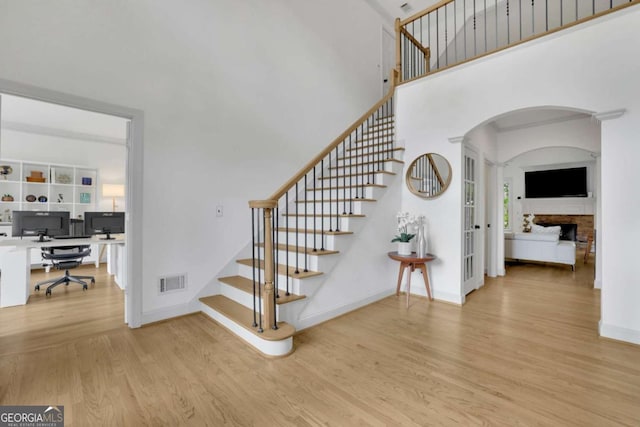 1025 Saint Marks Walk, Suwanee, GA 30024 - staircase featuring wood finished floors, a fireplace, arched walkways, a towering ceiling, and baseboards