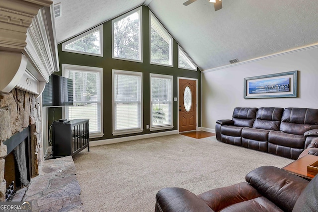 carpeted living room featuring high vaulted ceiling, a stone fireplace, plenty of natural light, a ceiling fan, and baseboards