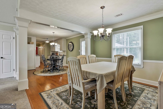 dining room with a chandelier, ornate columns, wood finished floors, baseboards, and a textured ceiling