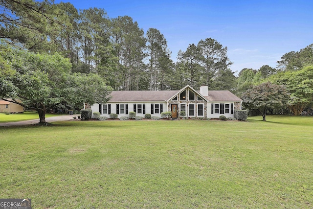 view of front facade with a front lawn, a chimney, and view of wooded area