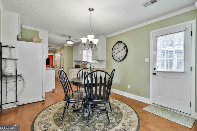 dining space with wood finished floors, a chandelier, crown molding, and baseboards