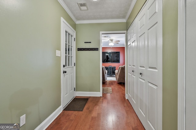 corridor with wood finished floors, crown molding, a textured ceiling, and baseboards