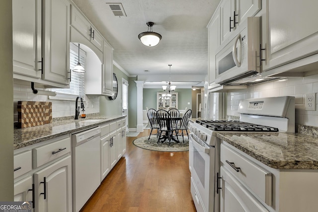 kitchen with white appliances, a sink, ornamental molding, a chandelier, and backsplash