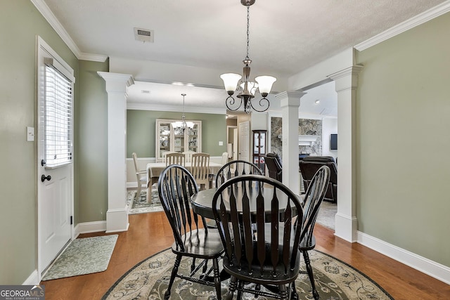 dining space with ornate columns, a chandelier, wood finished floors, baseboards, and ornamental molding