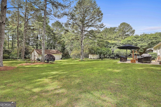 view of green lawn featuring a patio, a garage, and an outbuilding