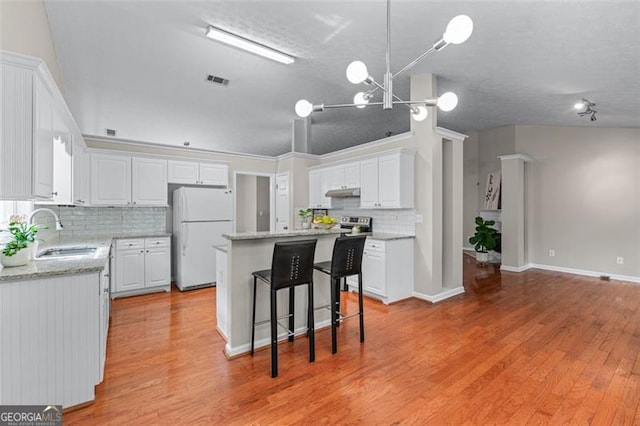 kitchen featuring a sink, freestanding refrigerator, white cabinets, tasteful backsplash, and a center island