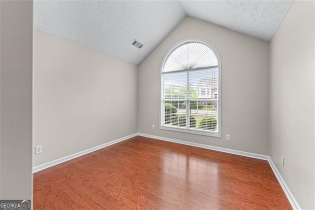 unfurnished room featuring lofted ceiling, wood finished floors, baseboards, and a textured ceiling