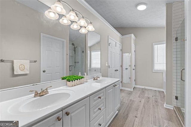 full bathroom featuring a stall shower, double vanity, wood finished floors, baseboards, and a textured ceiling