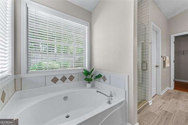 full bathroom with a bath, a stall shower, wood finished floors, and a spacious closet