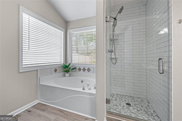 full bath featuring a shower stall, a bath, wood finished floors, vaulted ceiling, and baseboards