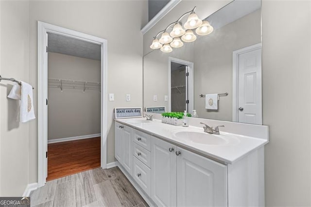bathroom featuring double vanity, wood finished floors, a walk in closet, and baseboards