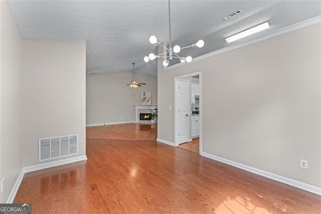 unfurnished living room with lofted ceiling, a ceiling fan, wood finished floors, a fireplace with flush hearth, and a chandelier