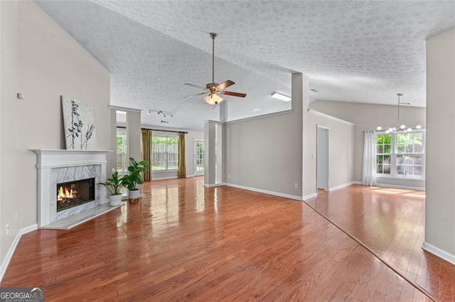 unfurnished living room with a ceiling fan, wood finished floors, baseboards, a tiled fireplace, and a textured ceiling
