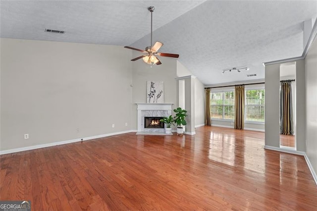 unfurnished living room with ceiling fan, a high end fireplace, wood finished floors, baseboards, and a textured ceiling